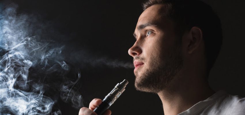 The face of vaping young man on black studio background